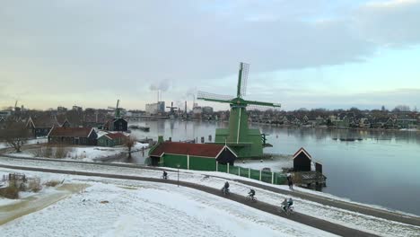 People-cycling-at-Zaanse-Schans-windmills,-flying-past-The-Crowned-Poelenburg