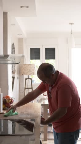 mature man cleaning the surface of a kitchen while his granddaughter playing
