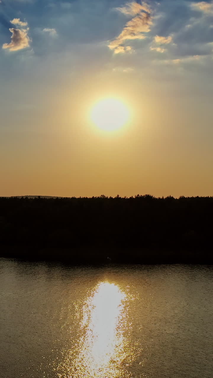 Beautiful evening view on the river at sunset. Golden path in the water from the setting sun on the natural landscape background. Aerial view. Motion camera back. Vertical video