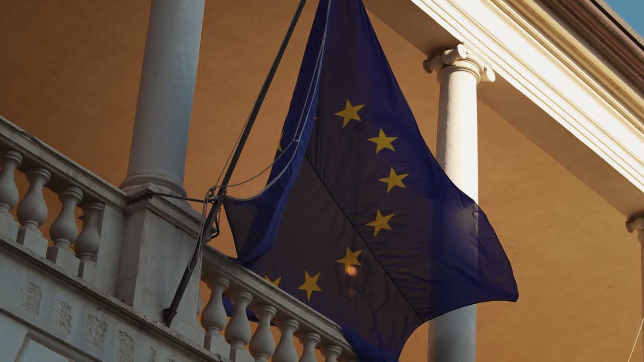 Bandiera dell'UE con stelle dorate che sventola al vento sulla facciata dell'edificio storico Palazzo Broletto, Brescia, Italia, al rallentatore.