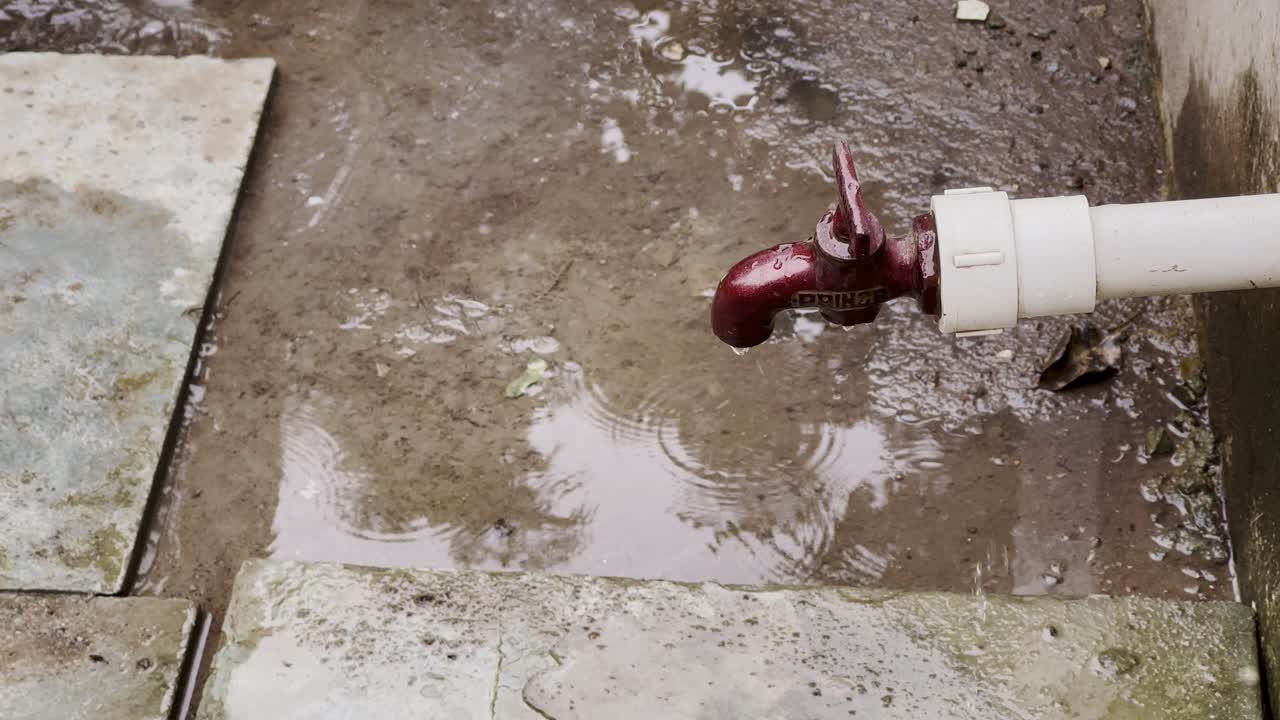 Closeup of a badly unfited tap making significant amount of water being wasted as it's dripping from the faucet's side, creating a puddle on the ground