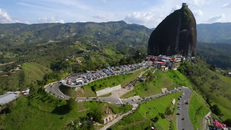 Lago-Guatape-Y-Roca-El-Peñol,-Vista-Aérea-Del-Paisaje-Verde,-Carretera,-Estacionamiento-Y-Punto-De-Referencia-En-Un-Día-Soleado,-Revelando-Un-Disparo-De-Drone