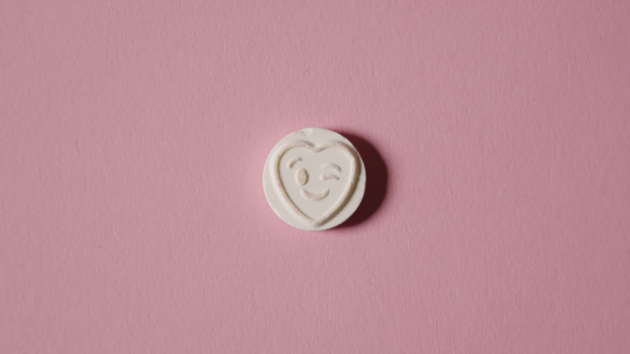 분홍색 배경에 윙크하는 이모티콘으로 하트 사탕을 손에 들고