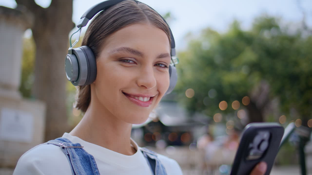 Earphones lady looking smartphone screen at sunny street closeup. Happy teenager