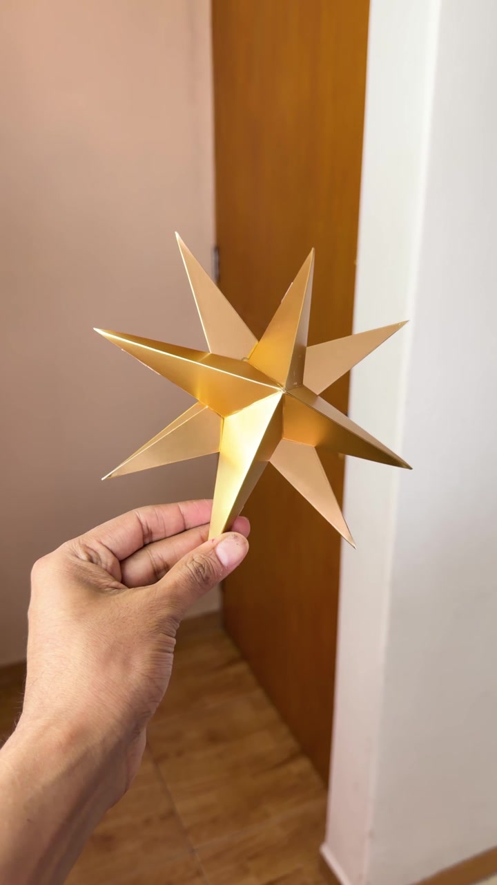 Mano che mostra un ornamento natalizio a forma di stella 3D color oro metallizzato all'interno, verticale ampia