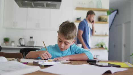 niño caucásico sentado en la mesa haciendo tareas escolares en casa