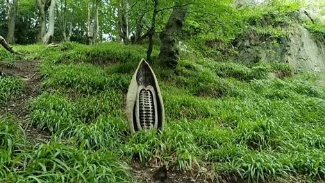 Unique-carved-wooden-sculpture-at-the-base-of-grassy-woodland-forest-hillside-slope