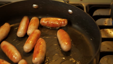 small chipolata sausages cooking in a stove top pan