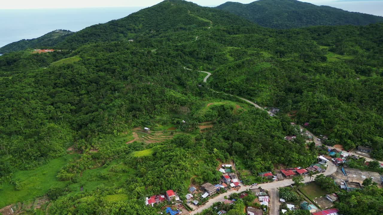 Aerial drone shot of hillside village community along lush tropical mountains with winding roads at Bato, Catanduanes, Philippines