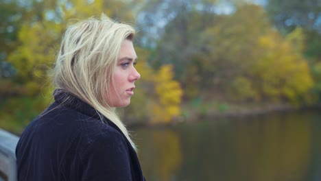 mujer de pelo rubio parada en el puente peatonal mientras mira hacia el río - tiro de cerca