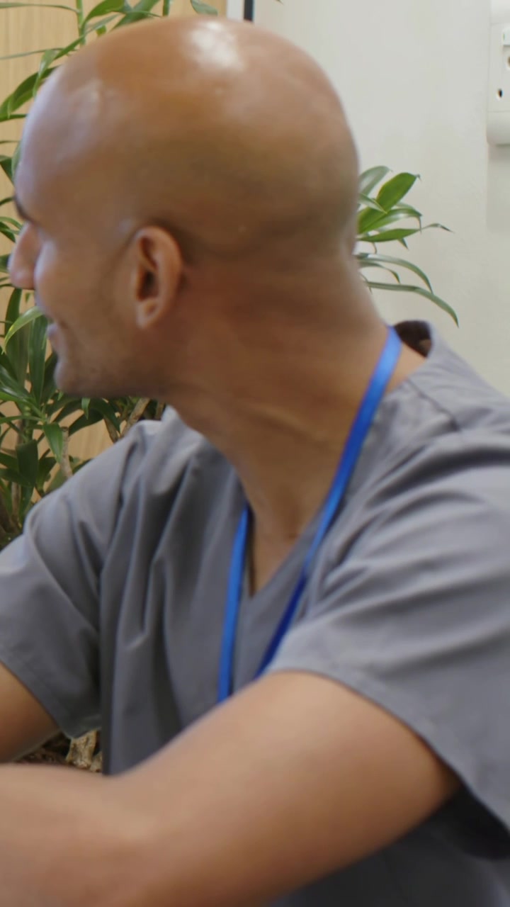 Vertikal video: Kliniker i arbeidsklær med blått ID-kort snur hodet og svarer på en oppfordring utenfor bildet på klinikken.