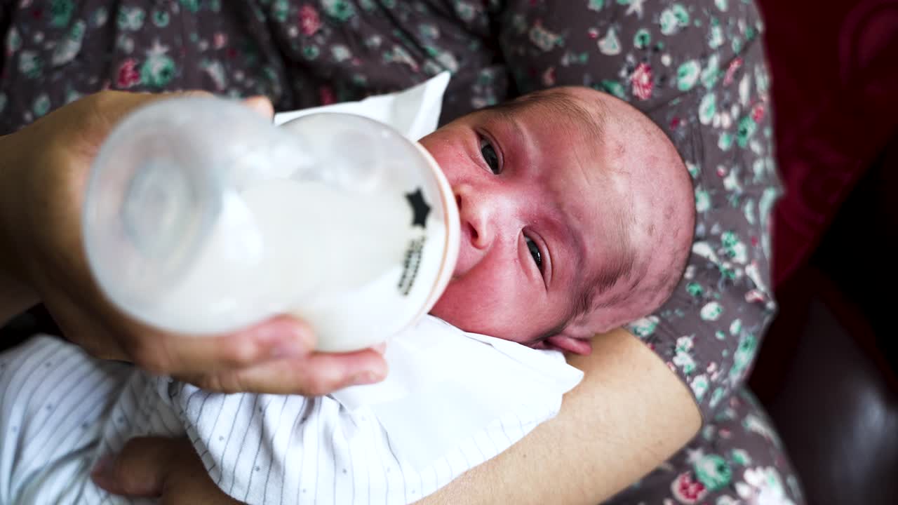 Adorabile primo piano di un neonato cullato tra le braccia della madre che si nutre con il biberon