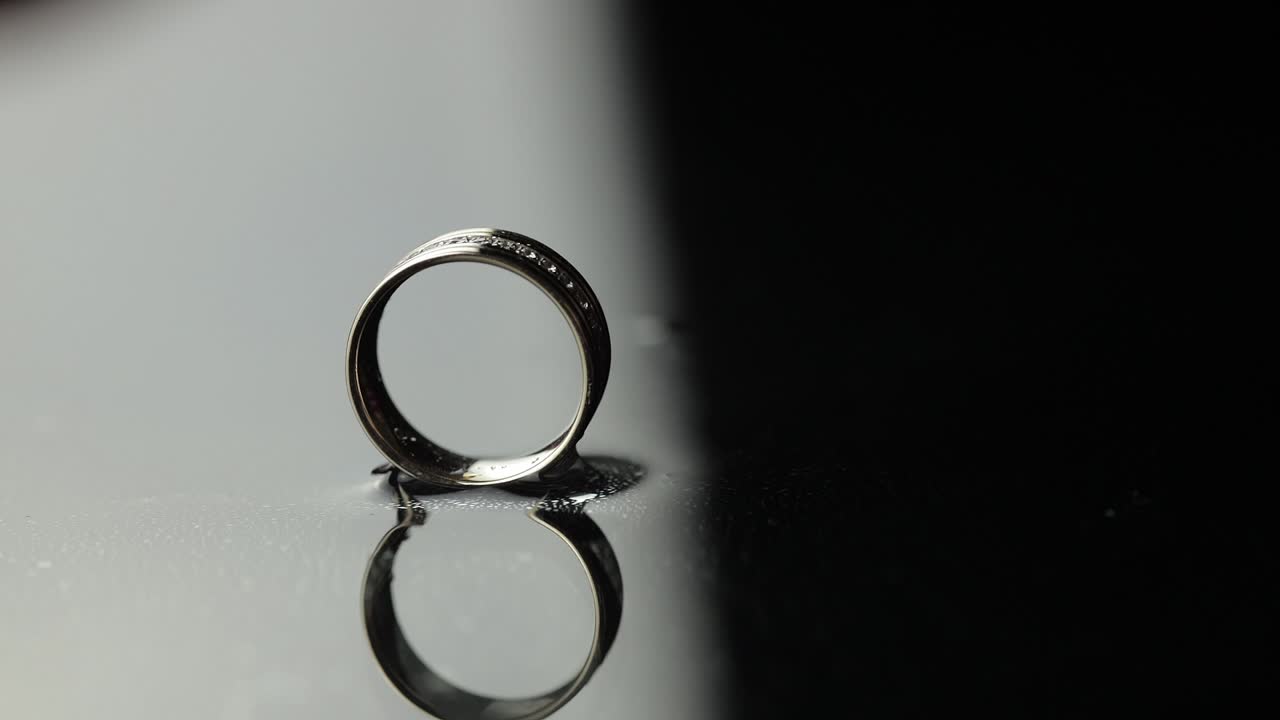 Wedding rings on black, white water surface. Groom ring rolling to bride's ring
