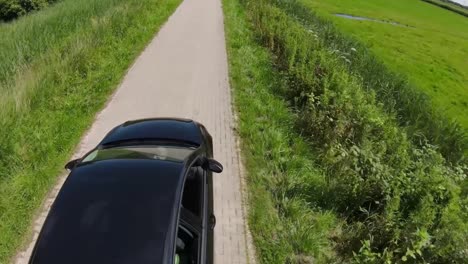 black car drives along a small path between fields