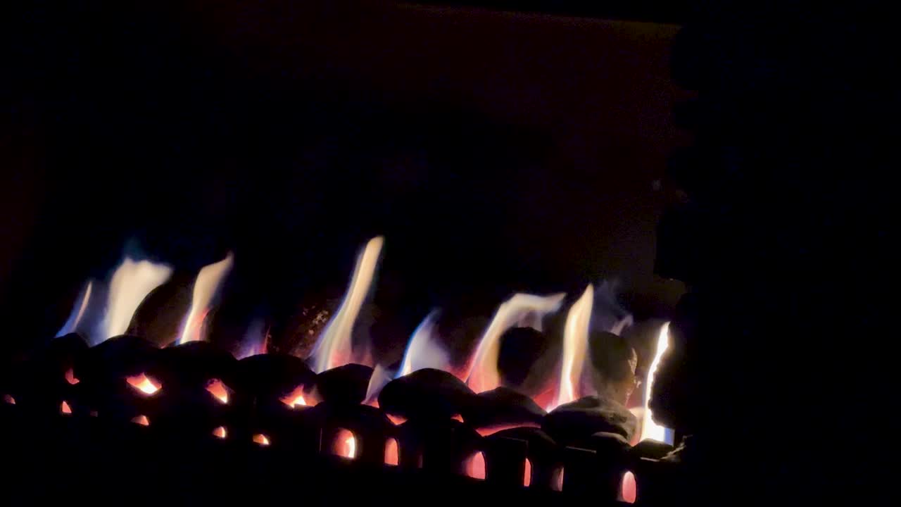 Steady camera captures flickering fireplace flames in a dark, cozy indoor setting with warm lighting
