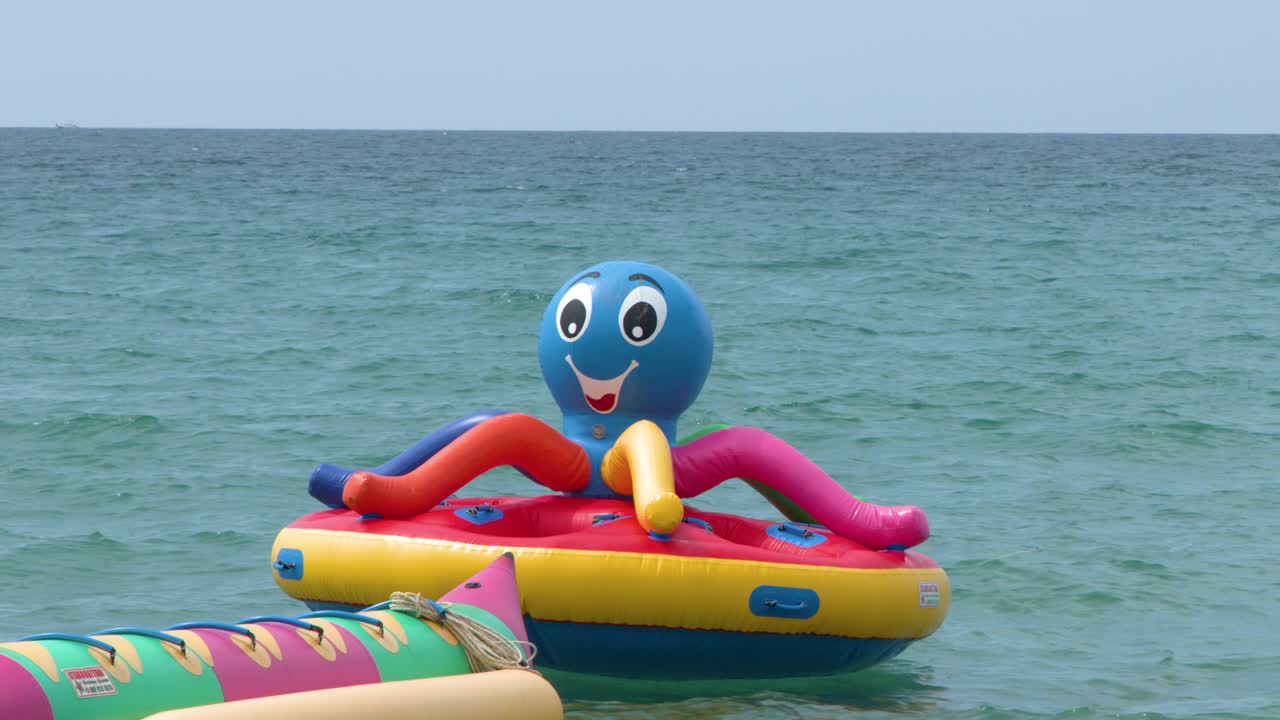 Static wide shot of vibrant inflatable water toys floating on calm turquoise tropical sea water