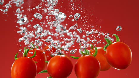 cherry tomatoes dropped into water making bubbles and sinking on red background, slow motion and macro