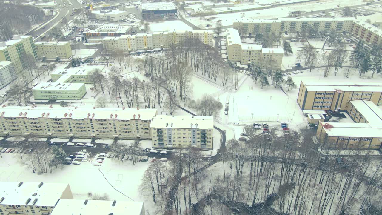 Aerial drone footage panning and showing soviet styled apartment complexes during a cloudy winter day with white fluffy snow covering the ground and rooftops. Cars parked and driving. Eastern europe.