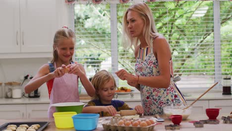 Happy-caucasian-mother-in-kitchen-with-daughter-and-son,-wearing-aprons-baking-cookies-together