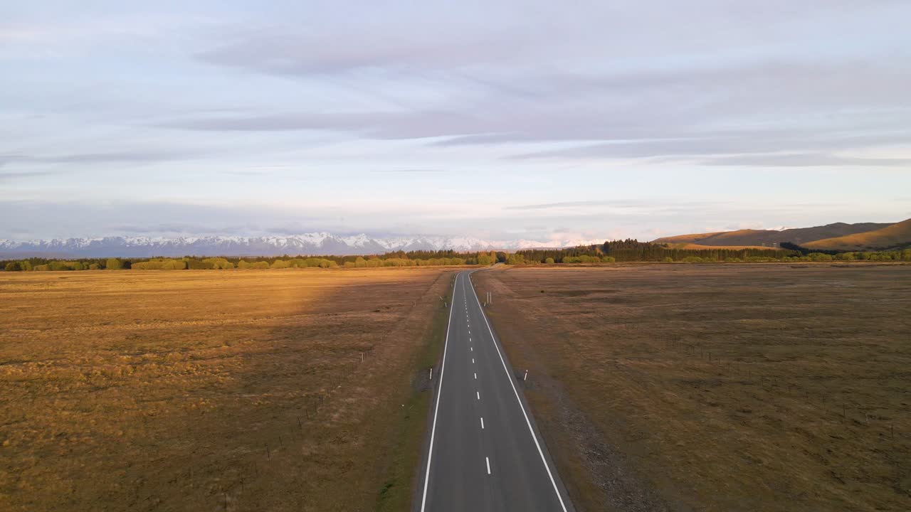 carretera rural recta que conduce a una impresionante cadena montañosa cubierta de nieve durante una hora dorada en canterbury, nueva zelanda