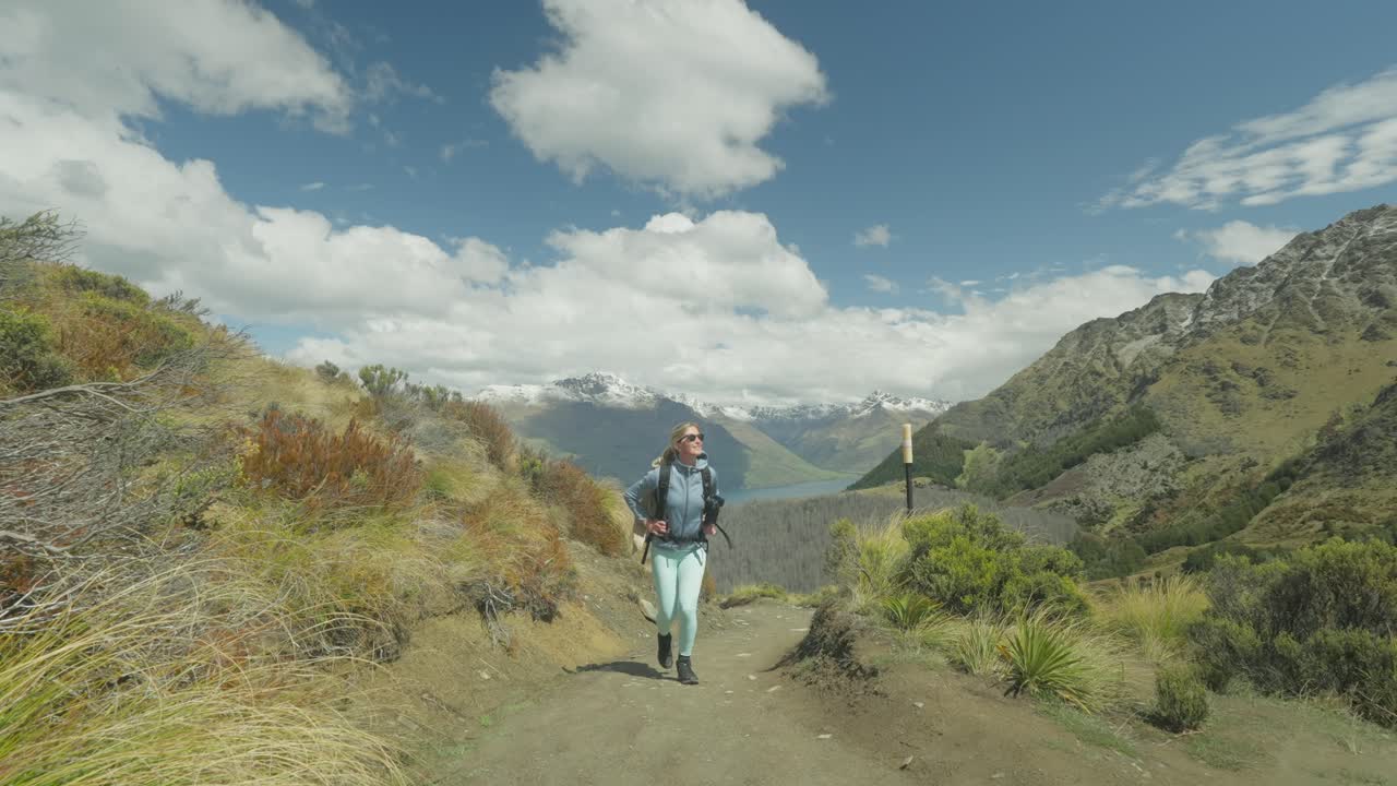 mujer en forma con mochila caminando por un sendero empinado de montaña en nueva zelanda