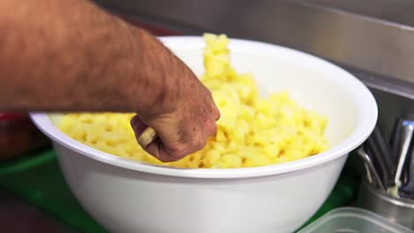 man stirring in slow motion with a wooden spatula a mass of cooked potato from a bowl