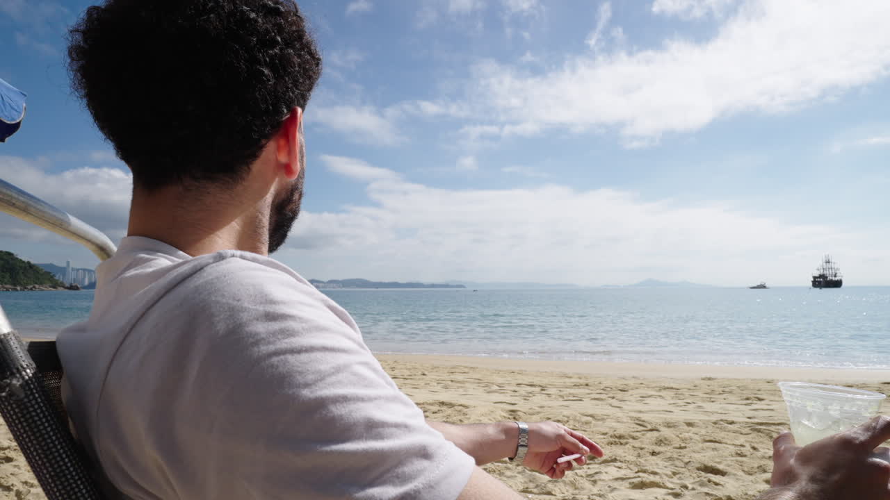 Close-up of man enjoying caipirinha cocktail while relaxing on sandy beach in Brazil