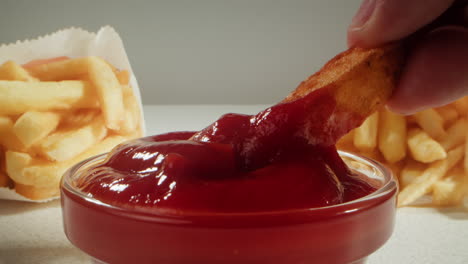 hand dipping french fries in ketchup