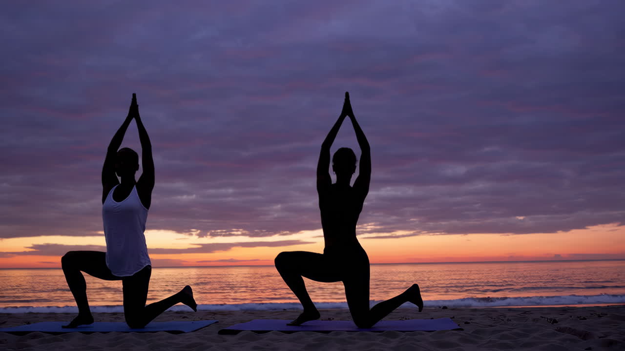 Women practicing yoga on a beach at sunrise/sunset