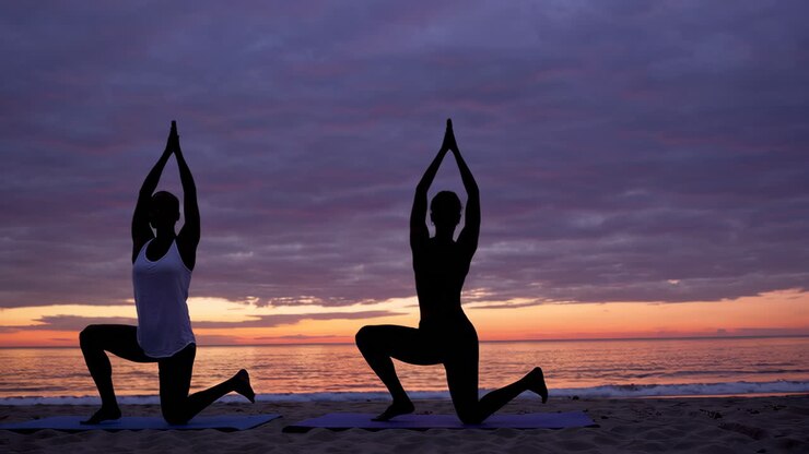 Women practicing yoga on a beach at sunrise/sunset