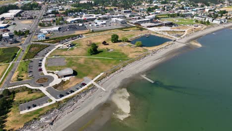 Aerial-view-of-Windjammer-Park-in-Oak-Harbor,-WA-with-the-bustling-city-off-in-the-distance