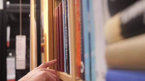 Hand-of-person-choosing-a-book-on-the-shelf-of-a-bookstore