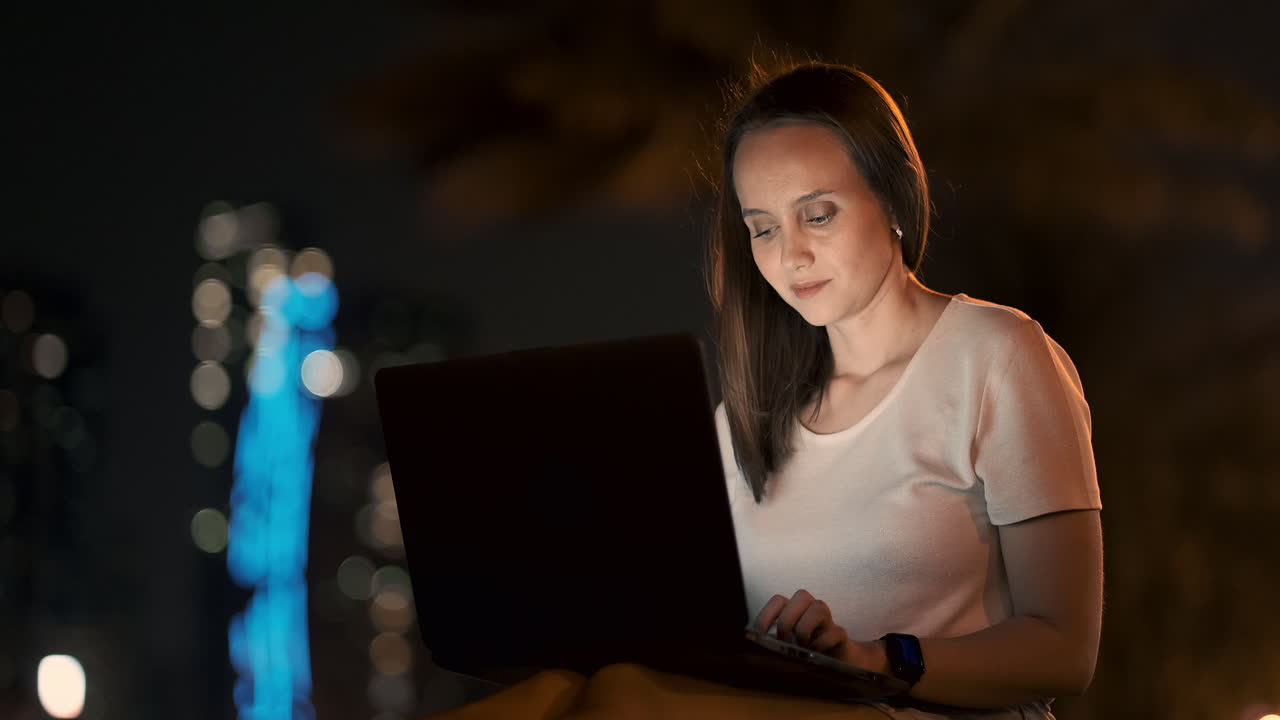 joven diseñadora hermosa trabajando remotamente en una computadora portátil en la calle en el verano bajo palmeras por la noche en el parque de la ciudad. emiratos árabes unidos mujer europea por la noite en dubai