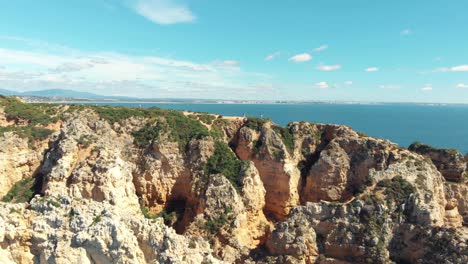 People-atop-weathered-headland-along-Ponta-da-Piedade,-Lagos,-Algarve,-Portugal---Aerial-Low-fly-over-shot