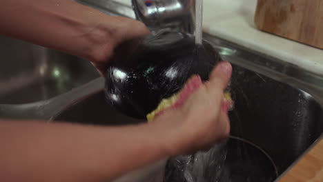 woman washes black bowl under tap water in a sink