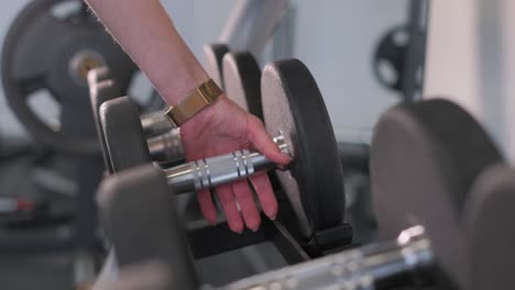 Person's Hand Picking Up a Dumbbell in a Gym