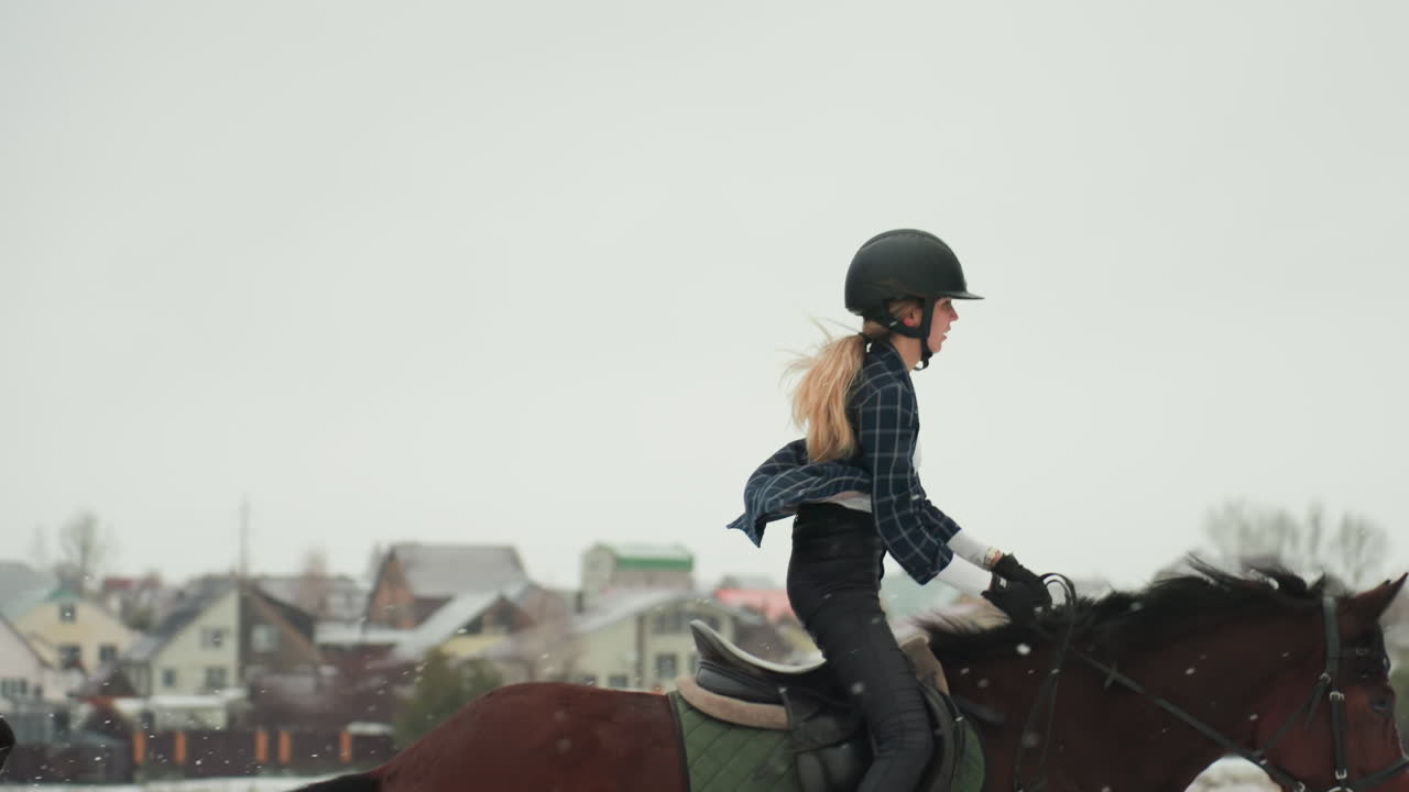 Un jeune cavalier maintient son équilibre et pratique sa posture dans un paysage enneigé. Cet étudiant caucasien se concentre sur sa tenue lors d'une promenade hivernale, s'exerçant avec détermination à une allure régulière en périphérie d'un village enneigé.