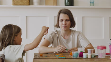 una niña rubia y su madre jugando con plastilina