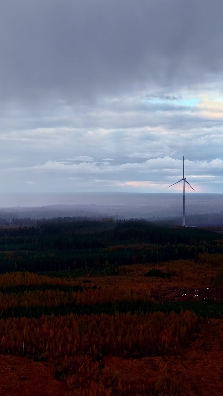 Vindmølle, der rejser sig gennem tåget landskab under en dramatisk skyet himmel, vertikal droneoptagelse, mens en regnfront bevæger sig hen over landskabet.