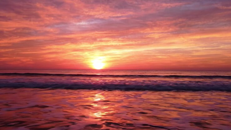 A Beautiful Sunset Over Tranquil Waters: Captivating Shades of Pink, Orange, and Purple Illuminate the Sky as Waves Gently Lapping the Shore Create a Serene Atmosphere.