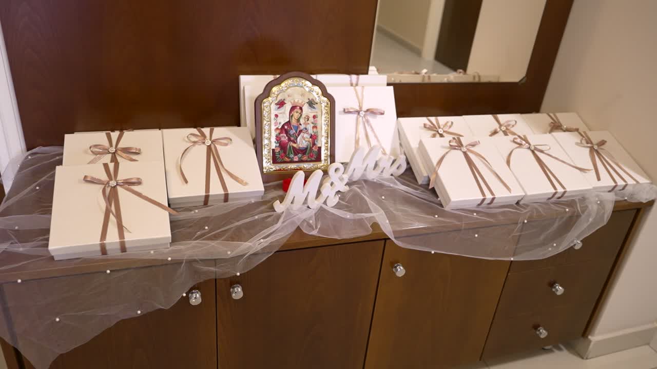 A table is set up with neatly arranged gift boxes tied with ribbons. An image of a saint is placed near the gifts, adding to the festive atmosphere