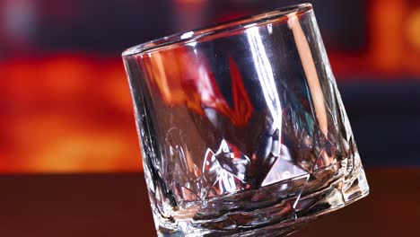 a sequence of an ice cube tilting inside a glass against a vibrant, fiery backdrop.