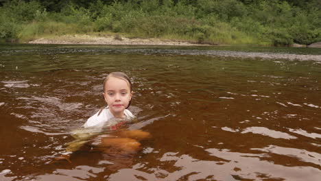 cute little girl sitting in a river jumps up and dives in, slow motion