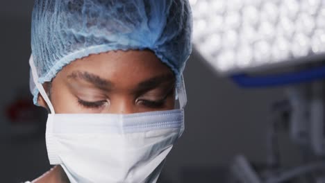 Portrait-of-african-american-female-doctor-wearing-face-mask-in-hospital-operating-room,-slow-motion