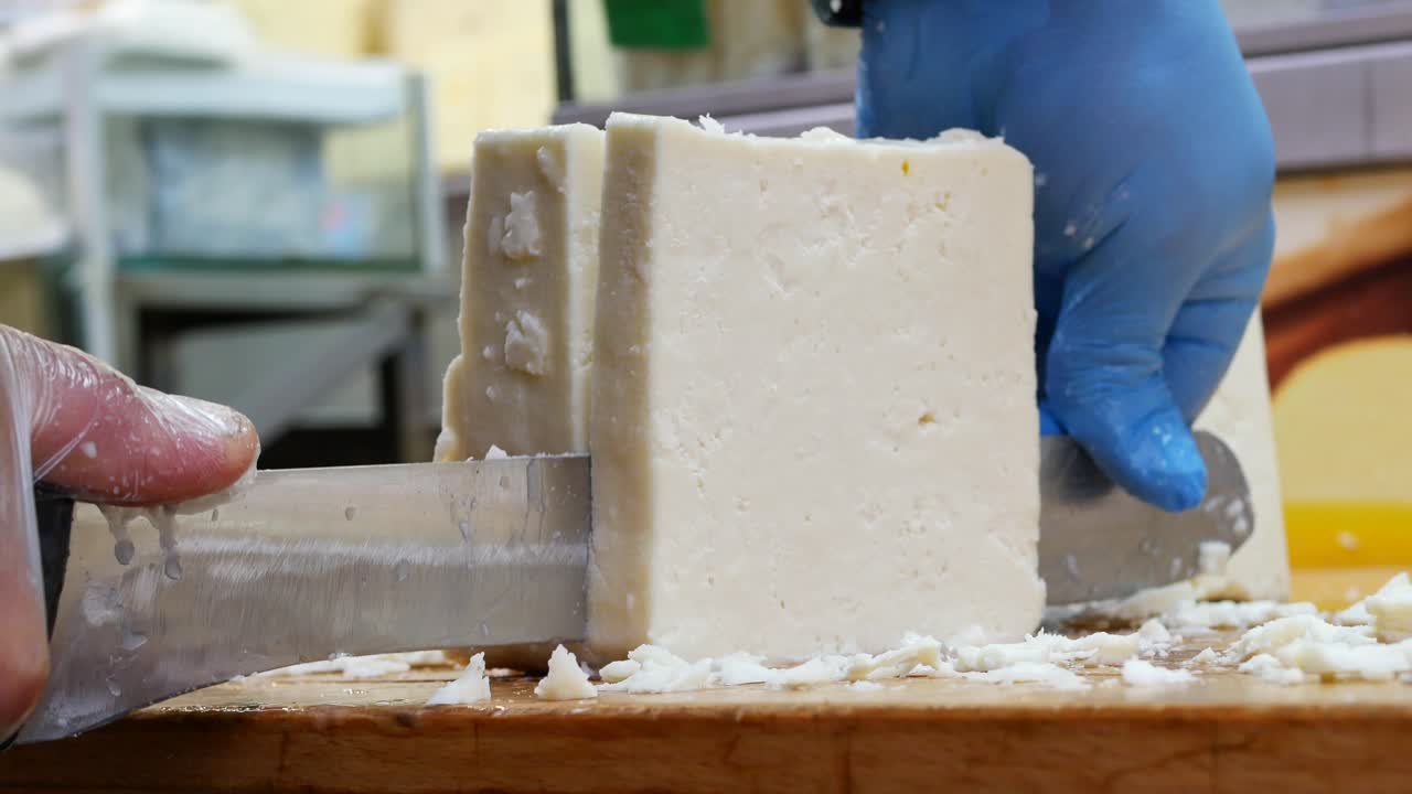 primer plano de manos cortando queso feta en una tabla de madera
