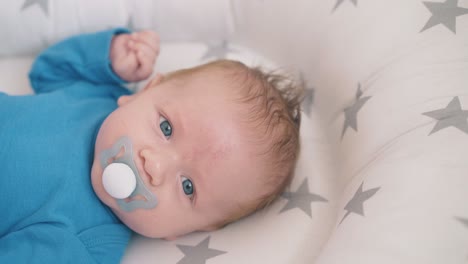 newborn boy with blue eyes sucks dummy in sleeping cocoon