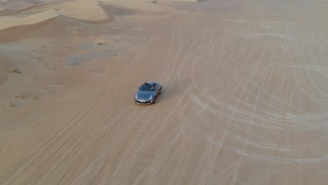 grey convertible car rides in the desert - distance drone following shot including epic dunes and sky