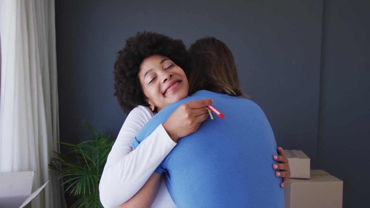 feliz pareja de raza mixta sosteniendo las llaves de la casa abrazándose en el nuevo apartamento