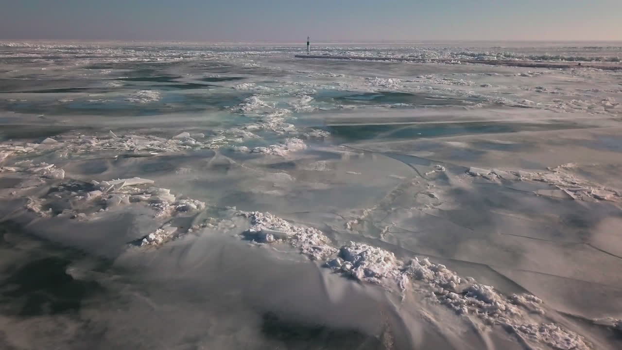 A lighthouse at the end of a pier in the middle of frozen icy lake Erie in winter