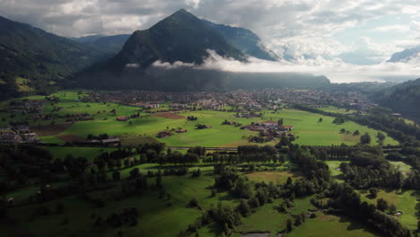 Opening-drone-shot-slowly-flying-towards-towering-mountains-with-lush-green-valleys-in-front